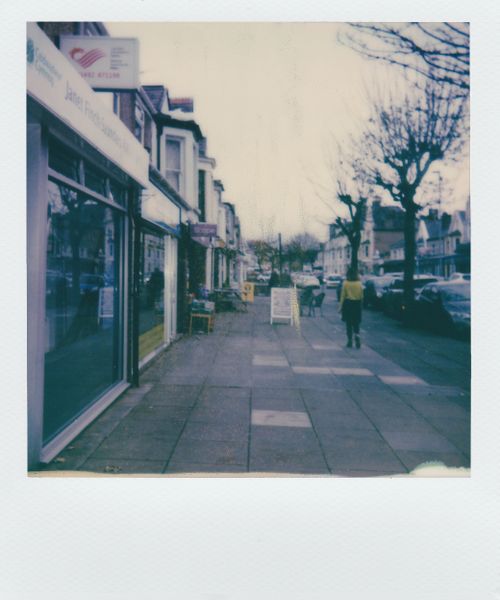 Free Retro polaroid capturing a quiet urban street scene with shops and sidewalk. Stock Photo