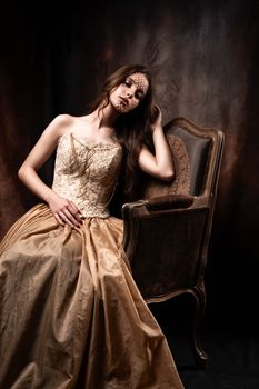 Elegant woman in a vintage dress seated by an ornate chair, exuding classic charm.