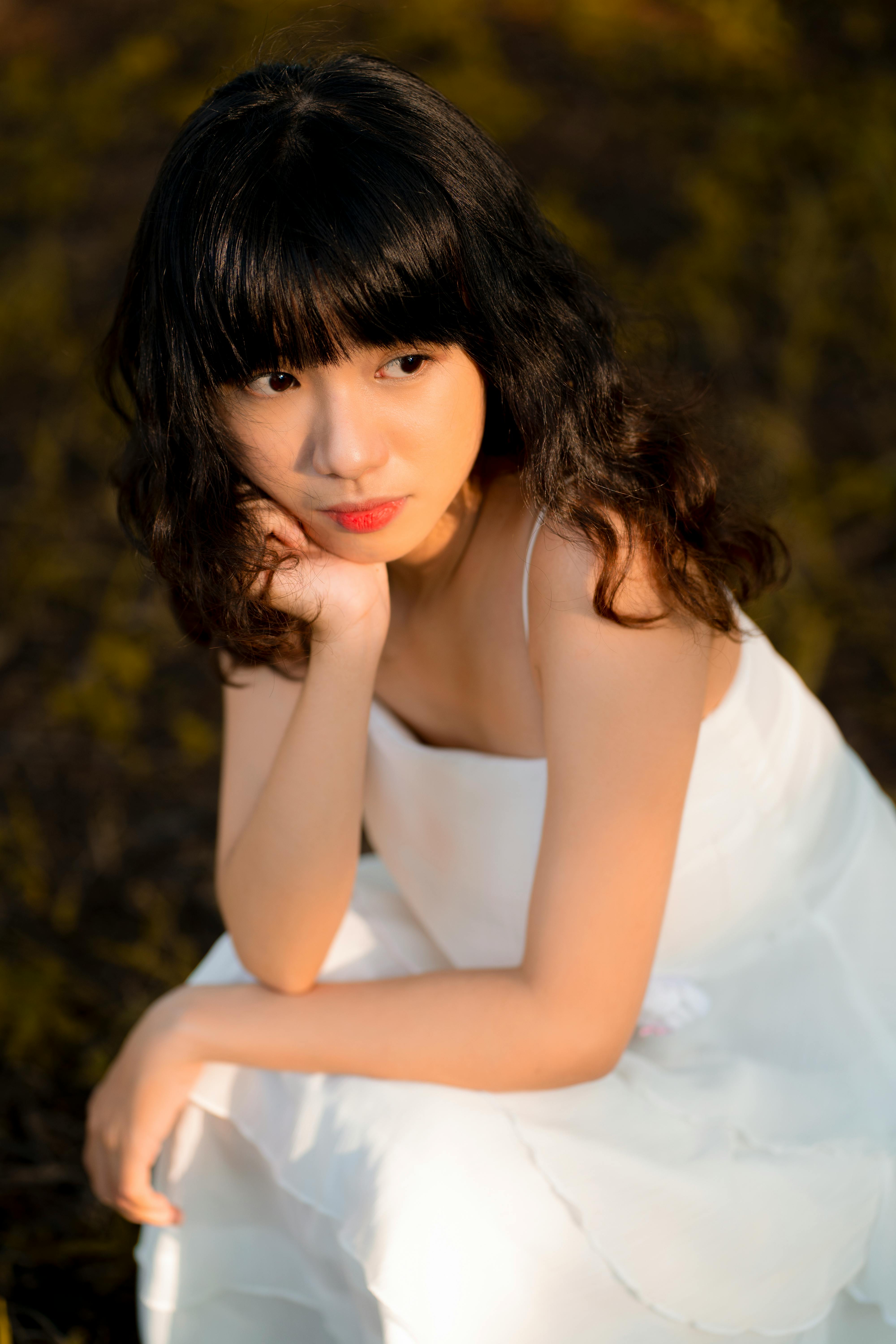 一位身着白色连衣裙的女子坐在户外，在温暖的阳光下若有所思地望向远方