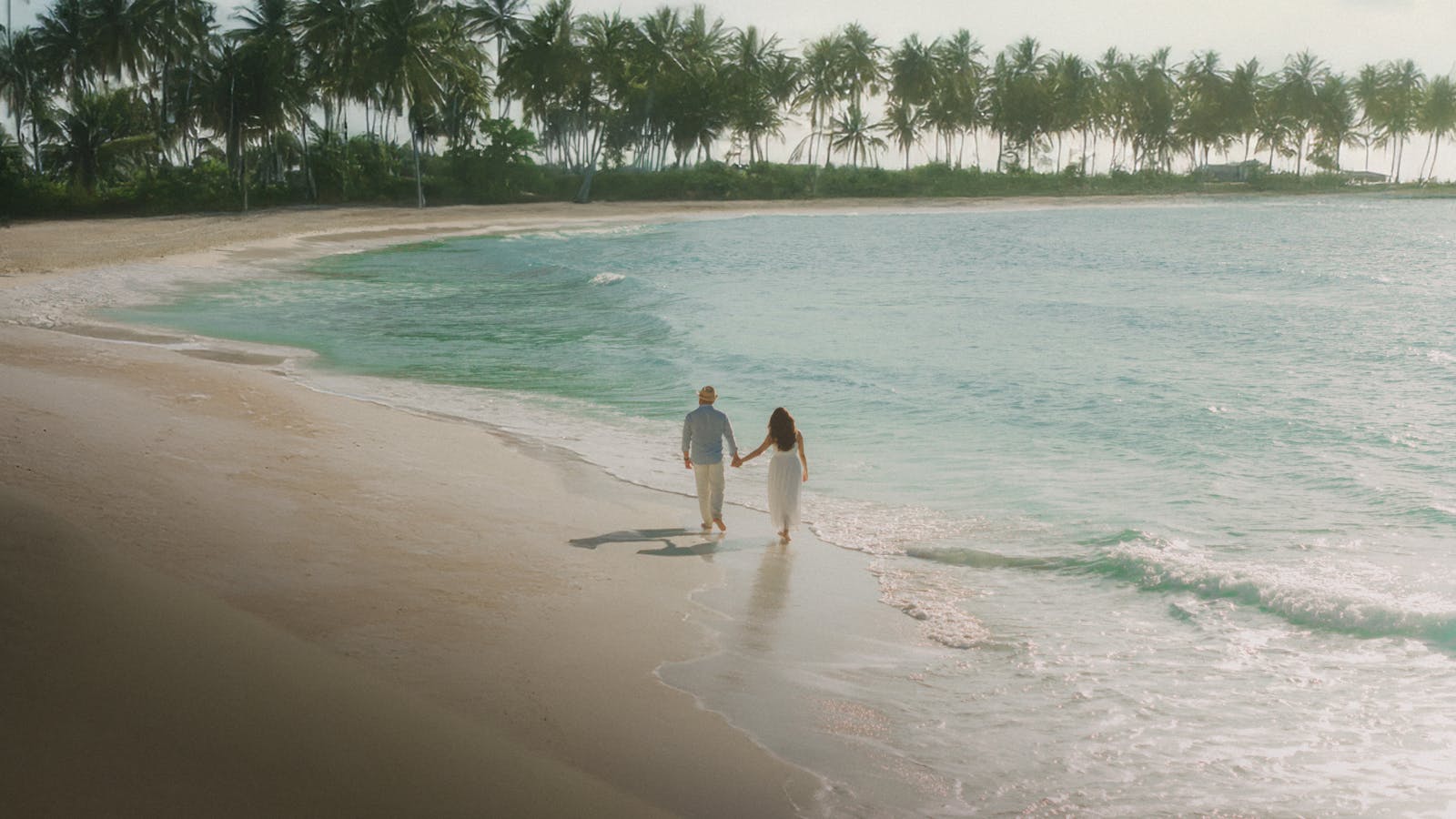 Couple se promenant sur une plage de Cancun, avec un ciel bleu et une ambiance romantique.