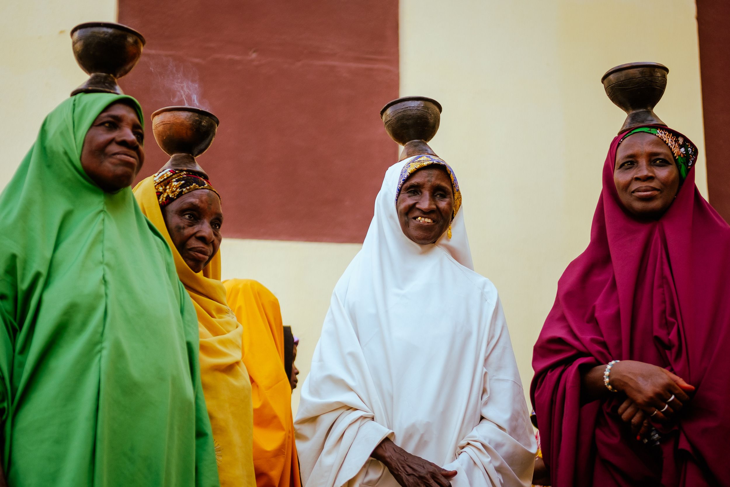 Women in vibrant traditional dresses balance pots on their heads in a cultural setting.