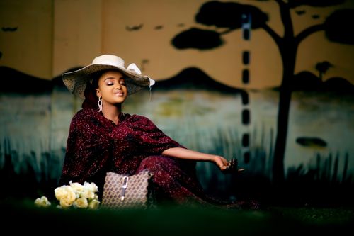 Free Woman enjoying a peaceful moment with flowers, wearing a hat and patterned dress. Stock Photo