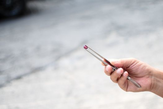 Close-up of a hand holding a gemstone with tweezers outside, highlighting precision and detail.