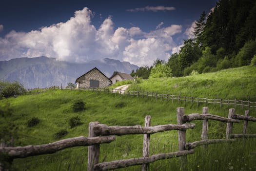 Beautiful rural landscape with green hills, wooden fence, and mountain backdrop.