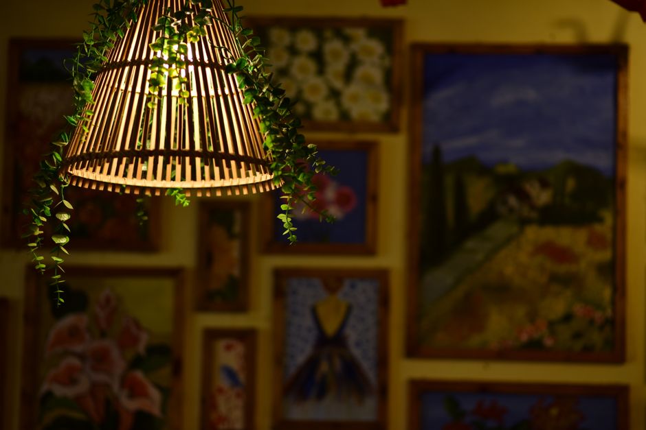 A warm rustic lamp with hanging greenery illuminates a cozy art gallery filled with vibrant, colorful paintings.