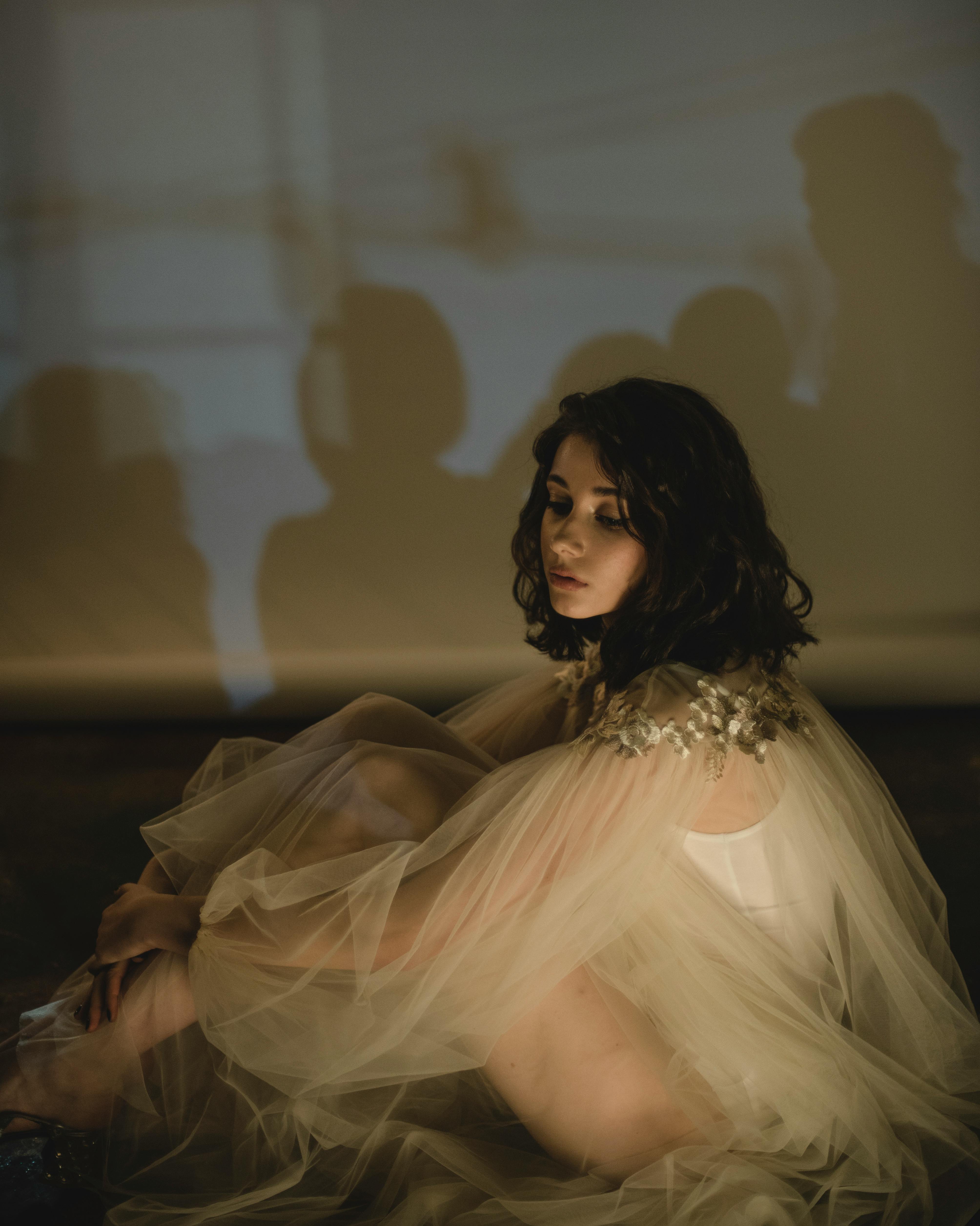 一位身着优雅礼服的女士在室内柔和的灯光下若有所思地摆着姿势