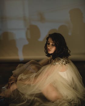 一位身着优雅礼服的女士在室内柔和的灯光下若有所思地摆着姿势