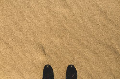 Free A lone pair of shoes on a textured sandy surface, creating a serene and minimalist composition. Stock Photo