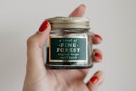 一只手持复古罐子，罐内是松树林香味蜡烛的时尚特写