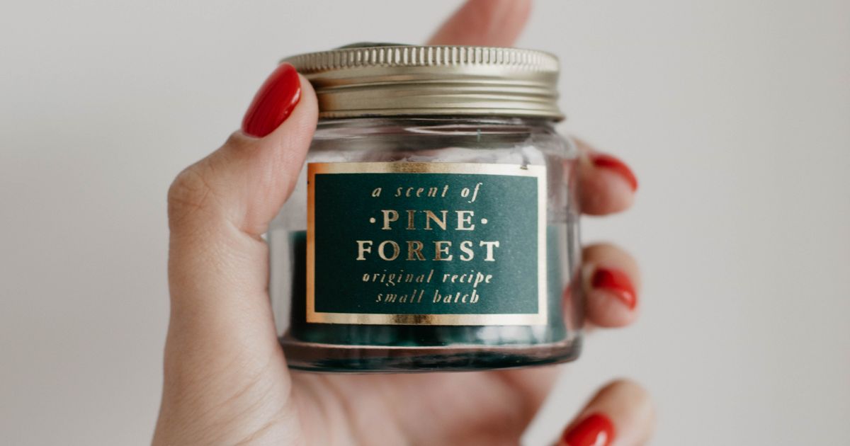 Hand holding a small batch pine forest scented candle in a glass jar