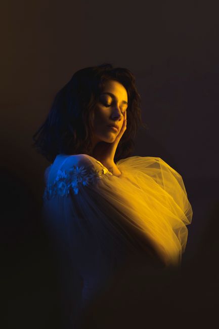 Artistic portrait of a woman in soft, dramatic lighting with a contemplative pose.