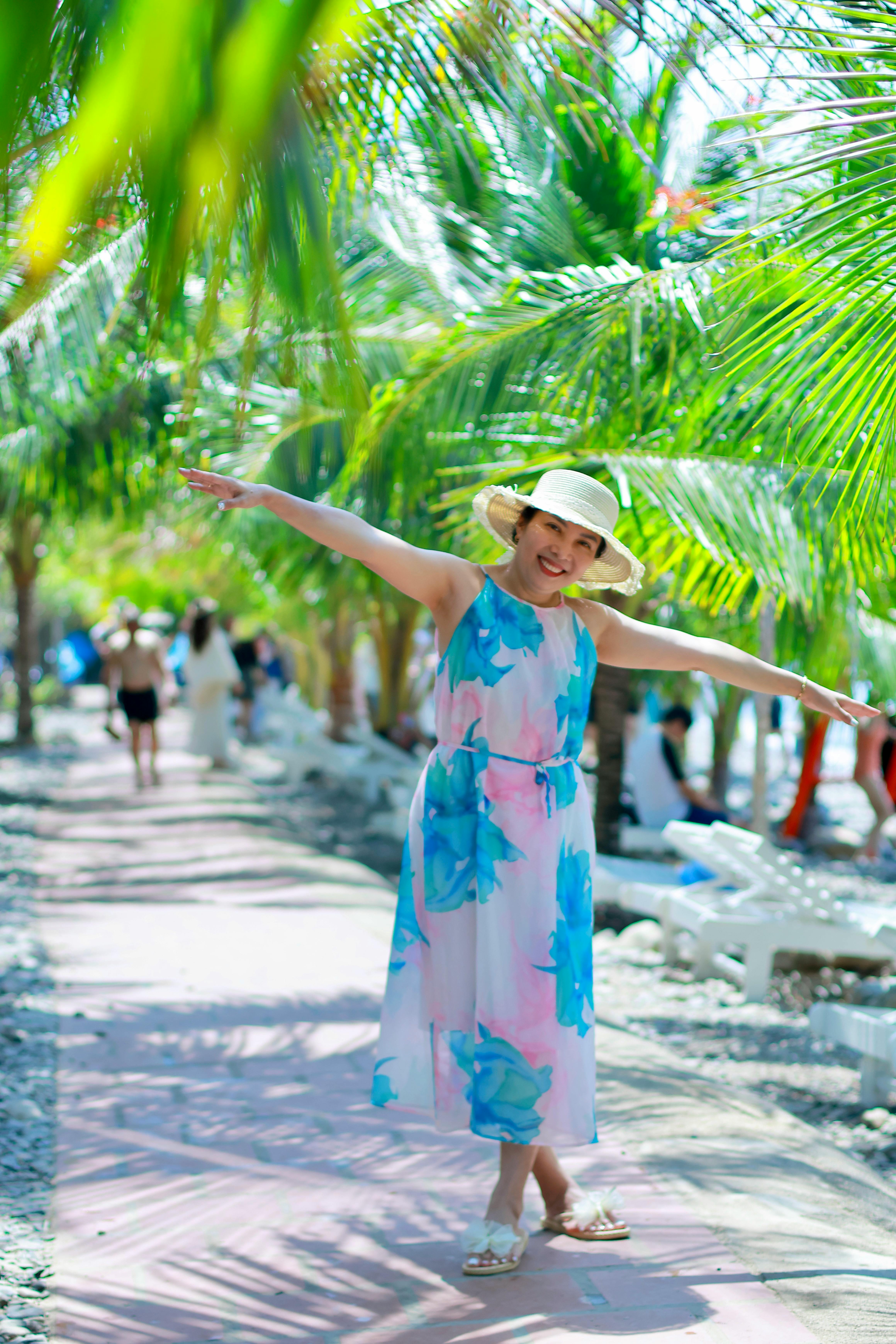 Free A smiling woman enjoying a sunny day at a tropical beach with palm trees. Stock Photo