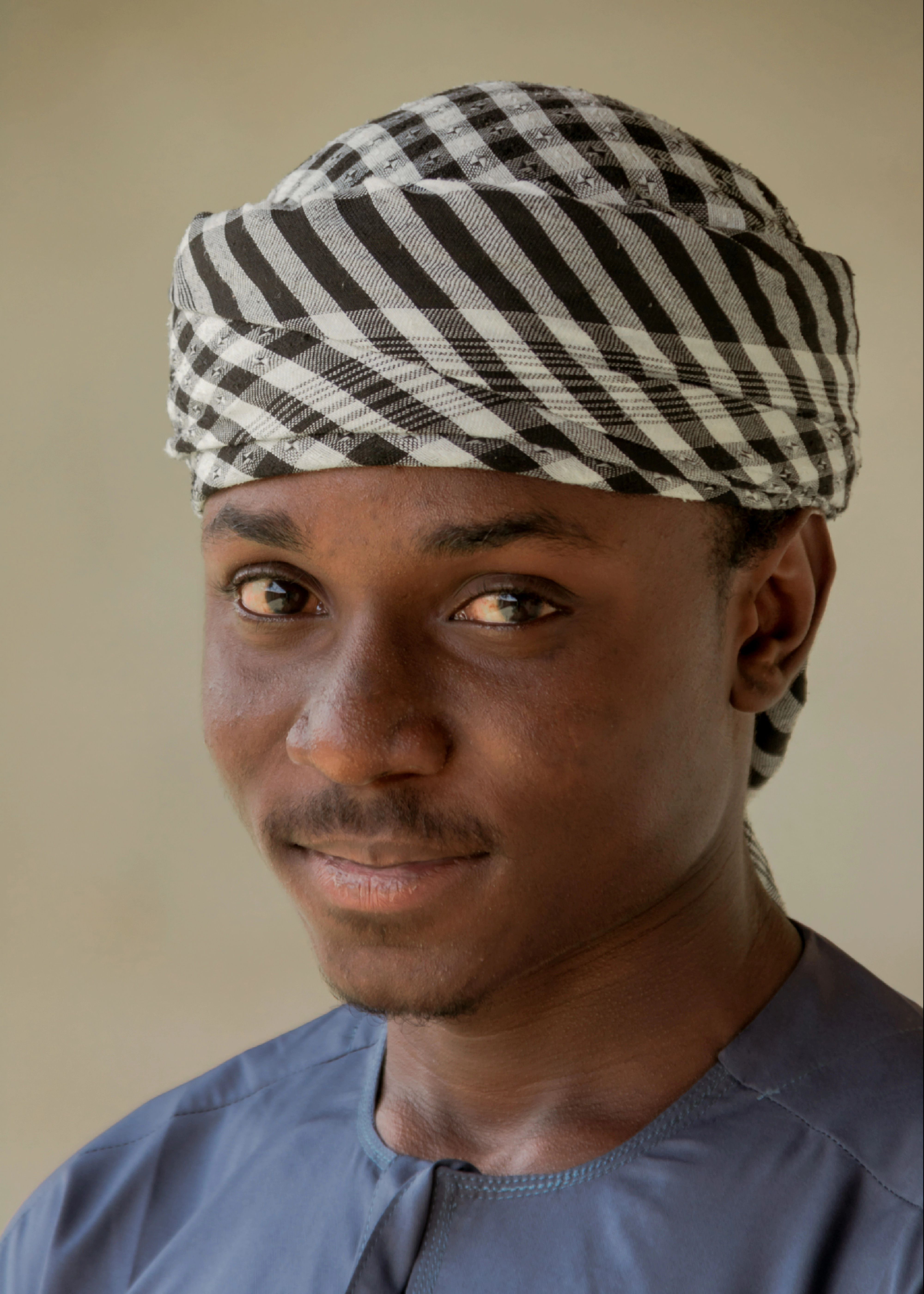 Close-up portrait of a young man wearing a striped headscarf with a subtle smile.