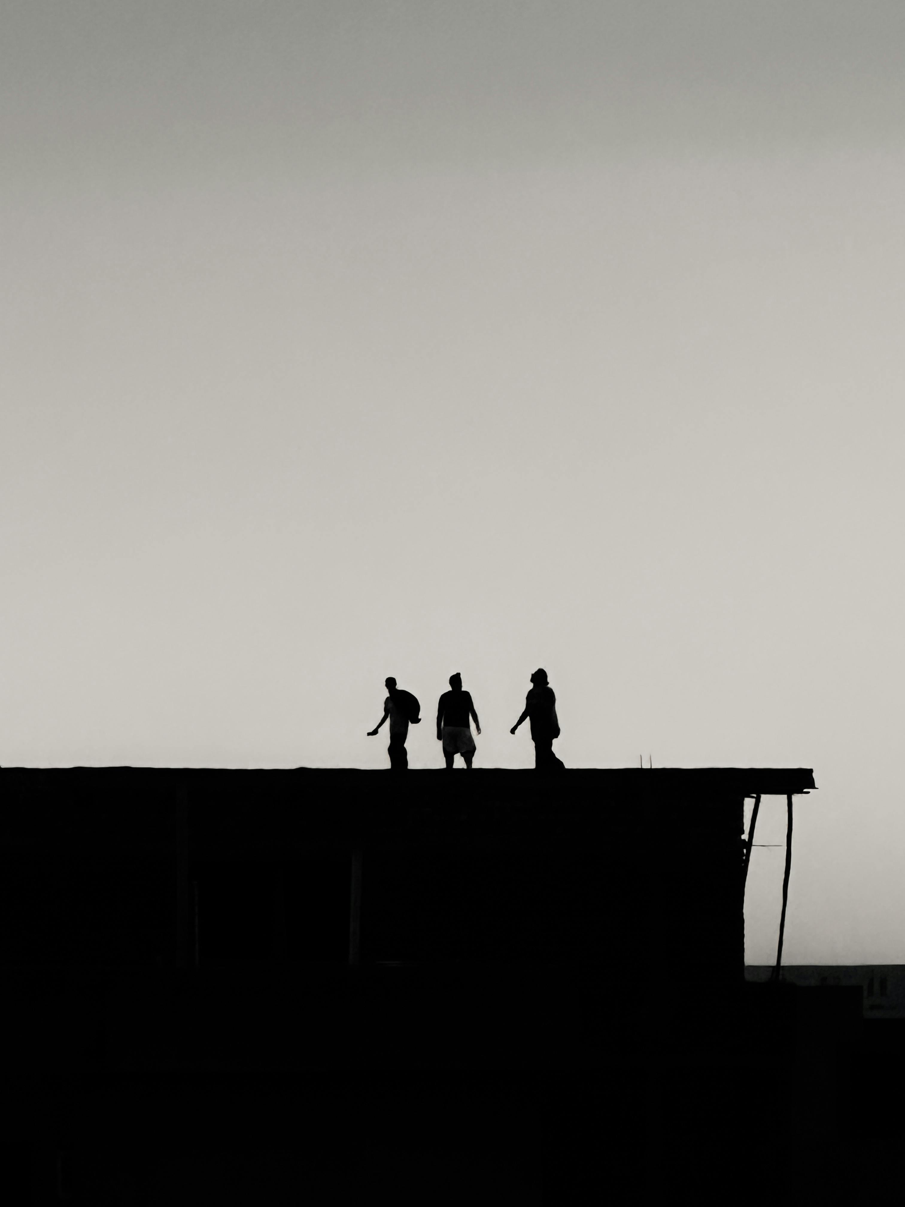 grátis Três figuras silhuetas caminham no telhado ao anoitecer, criando uma cena urbana dramática. Foto profissional