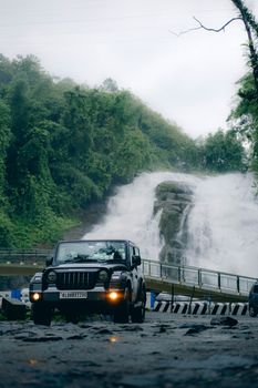 A jeep parked in front of a stunning waterfall in Kerala, surrounded by lush greenery.