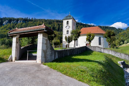 A picturesque Swiss church nestled in a lush valley against a mountain backdrop on a clear summer day.