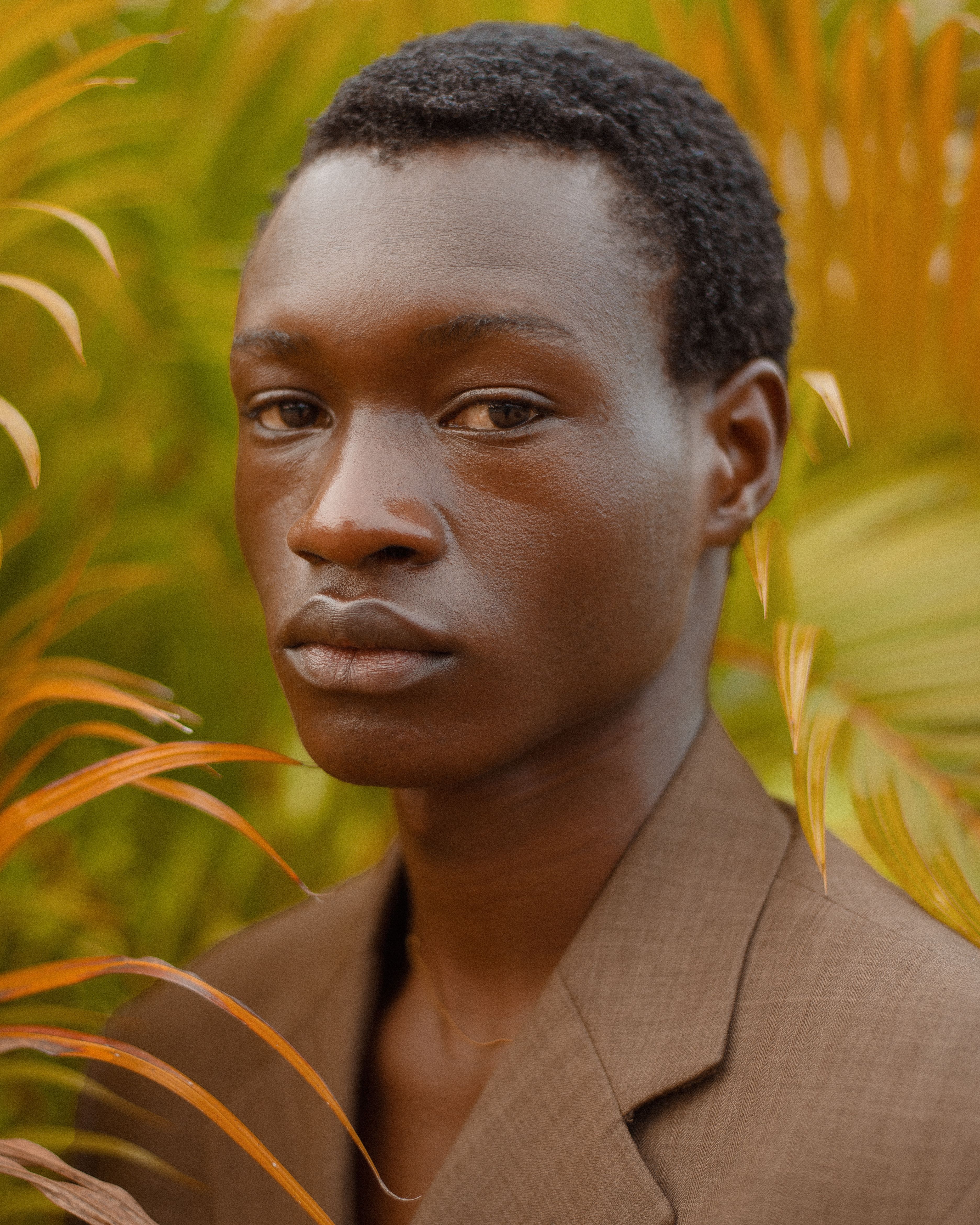 A stylish portrait of a young man surrounded by lush greenery.