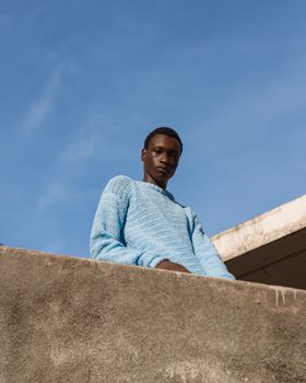 Portrait of a young man standing outdoors, wearing a blue sweater against a clear sky backdrop.