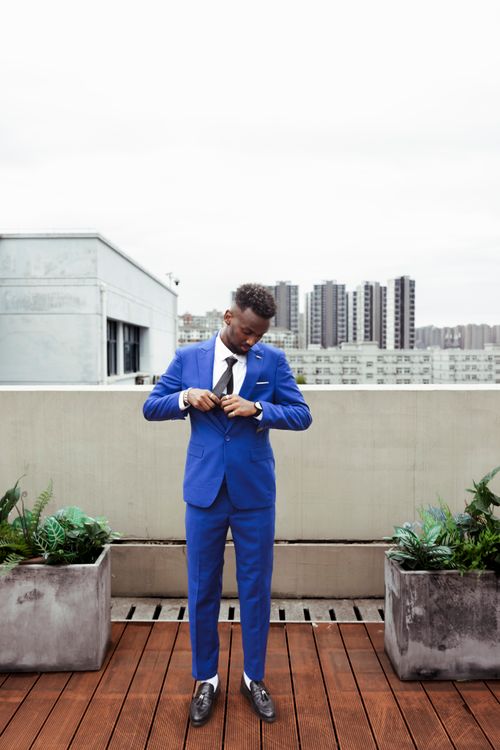Free Adult man in blue suit adjusting cuffs on a rooftop terrace with cityscape view. Stock Photo