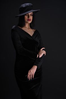Stylish portrait of a woman in a black dress and wide-brimmed hat against dark background.