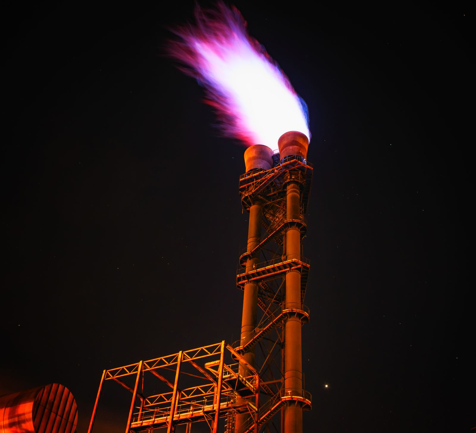A gas flare burning against a night sky at an industrial facility