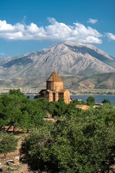 Stunning view of an ancient Armenian church set against a towering mountain and lush greenery.