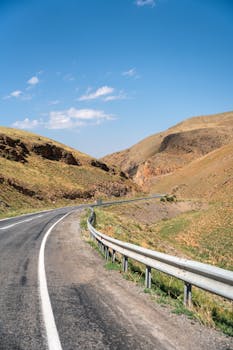 Curved mountain road under clear blue sky with distant rolling hills.