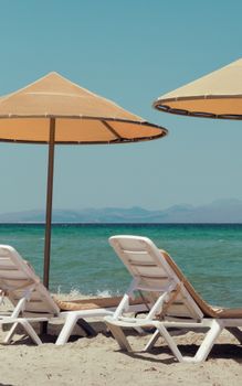 Relaxing tropical beach view with sun loungers and umbrellas under a clear blue sky.