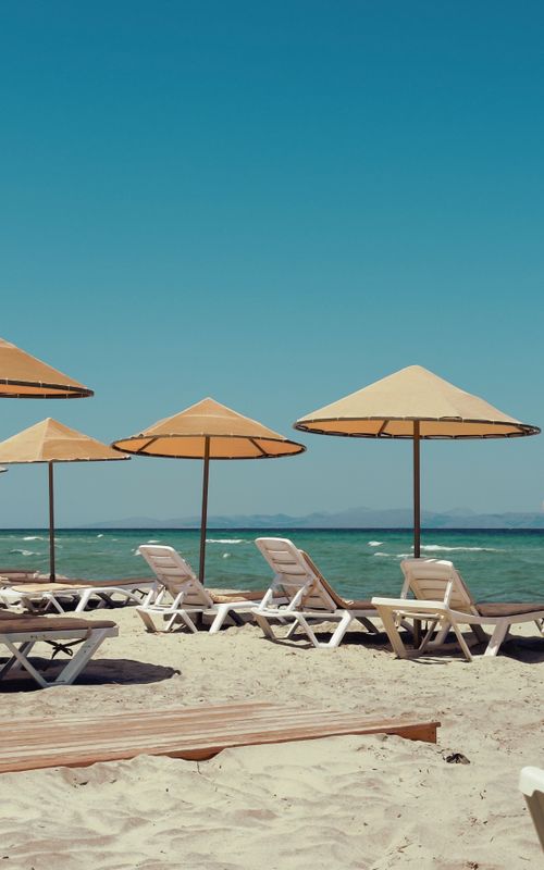 Free Idyllic beach scene with sun loungers and umbrellas under a clear blue sky, perfect for a summer escape. Stock Photo