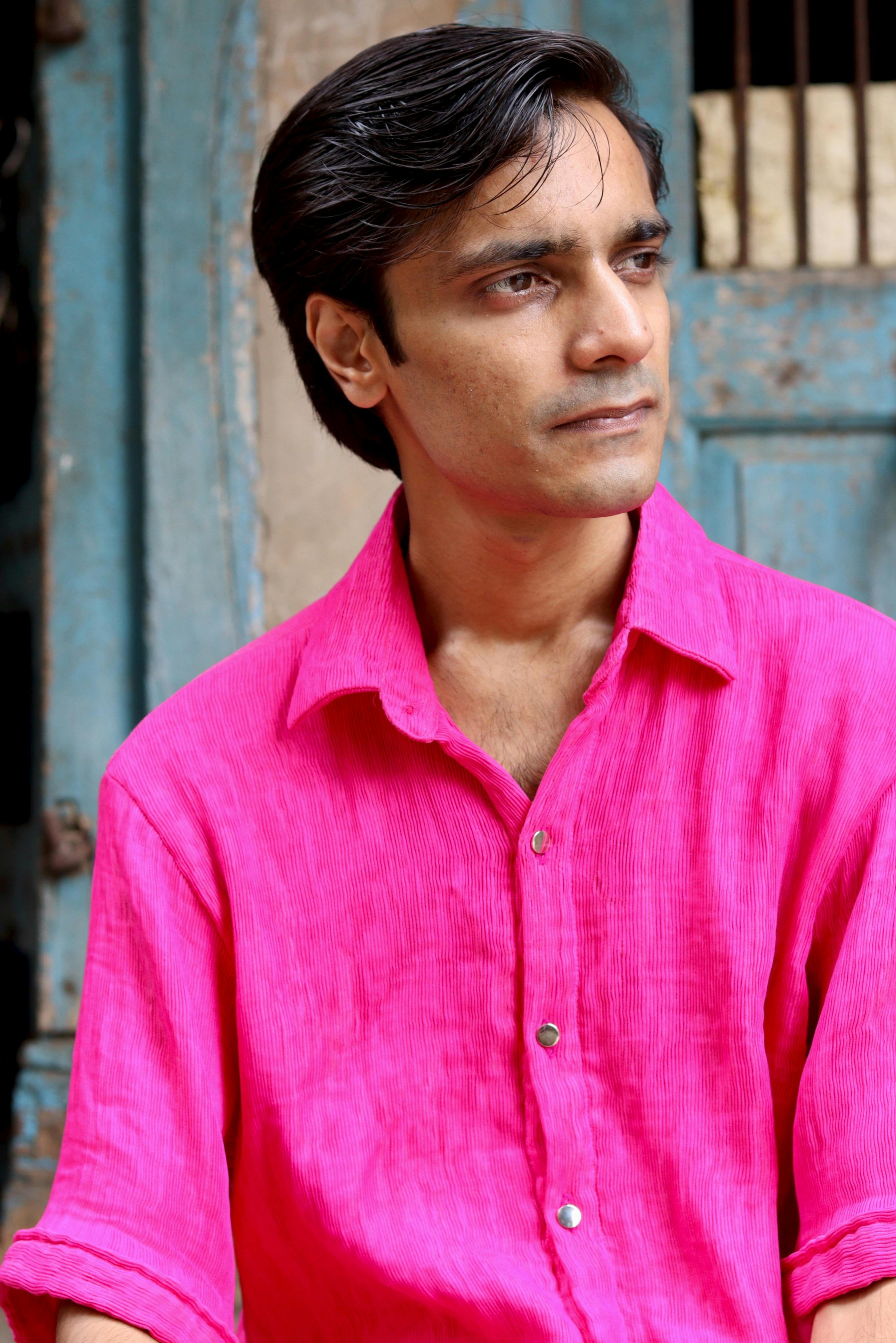 Portrait of a man in a vibrant pink shirt looking thoughtful outdoors.