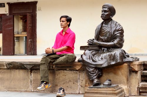 Free A man in a bright shirt sits beside a historical statue outdoors, reflecting deep in thought. Stock Photo