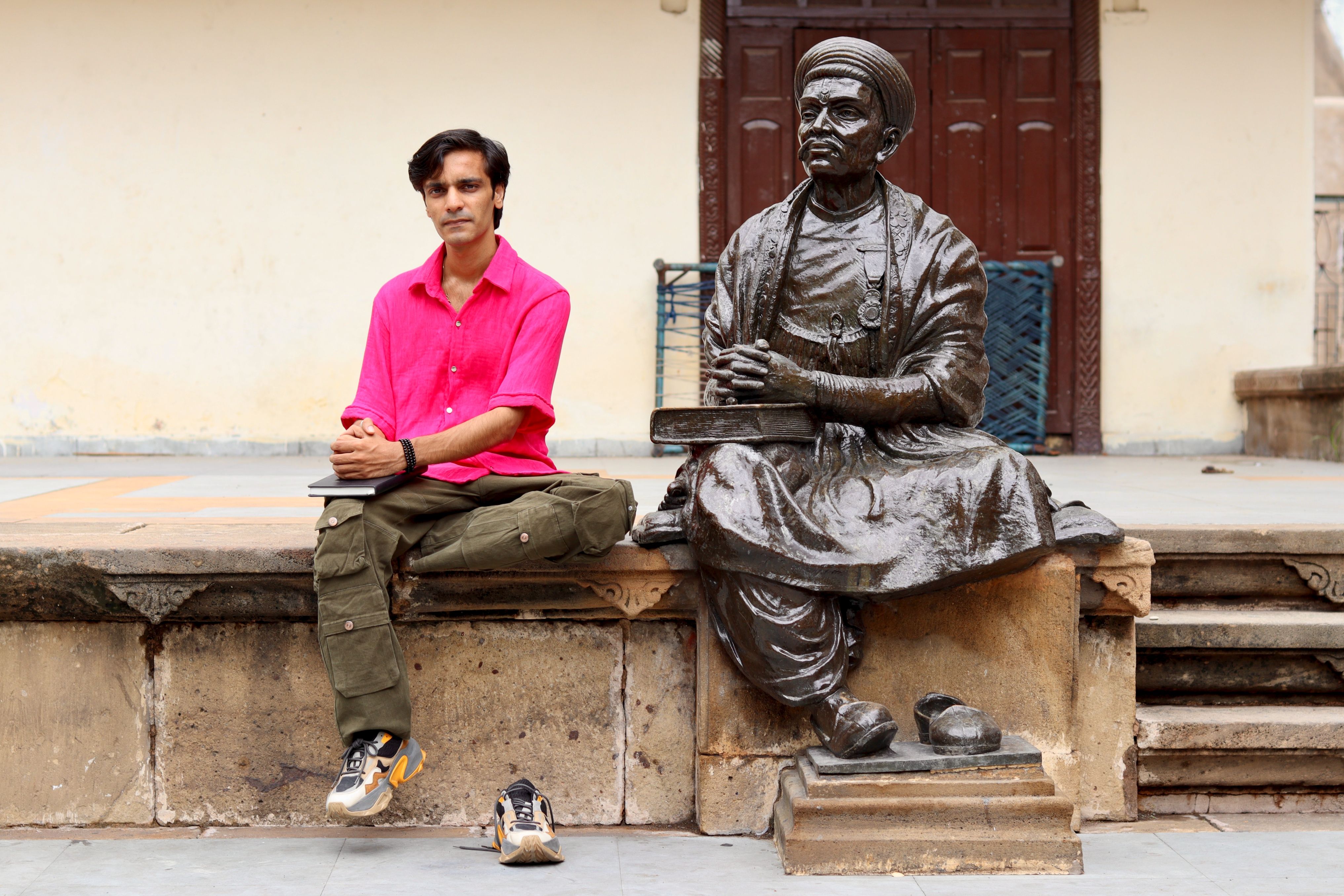 A man seated beside a bronze statue of a historical figure in an outdoor setting.