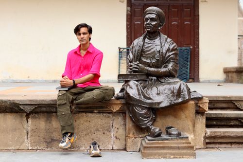 Free A man seated beside a bronze statue of a historical figure in an outdoor setting. Stock Photo