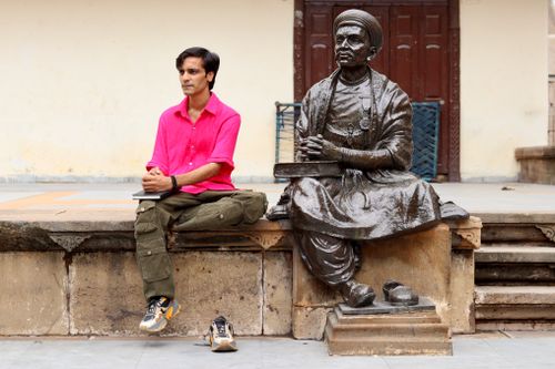 Free A man in a bright pink shirt sits beside a historical statue. Urban street scene. Stock Photo