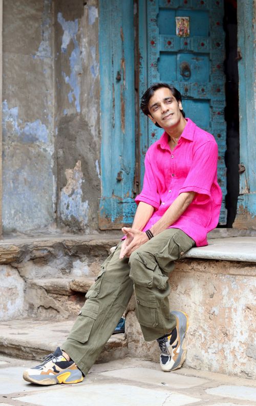 Free Man in bright pink shirt sitting on steps by a rustic blue door, casual urban setting. Stock Photo