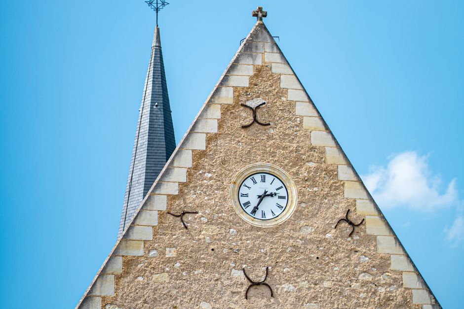 Close-up of a historic church tower with a clock in Pays de la Loire, France, under a clear blue sky.