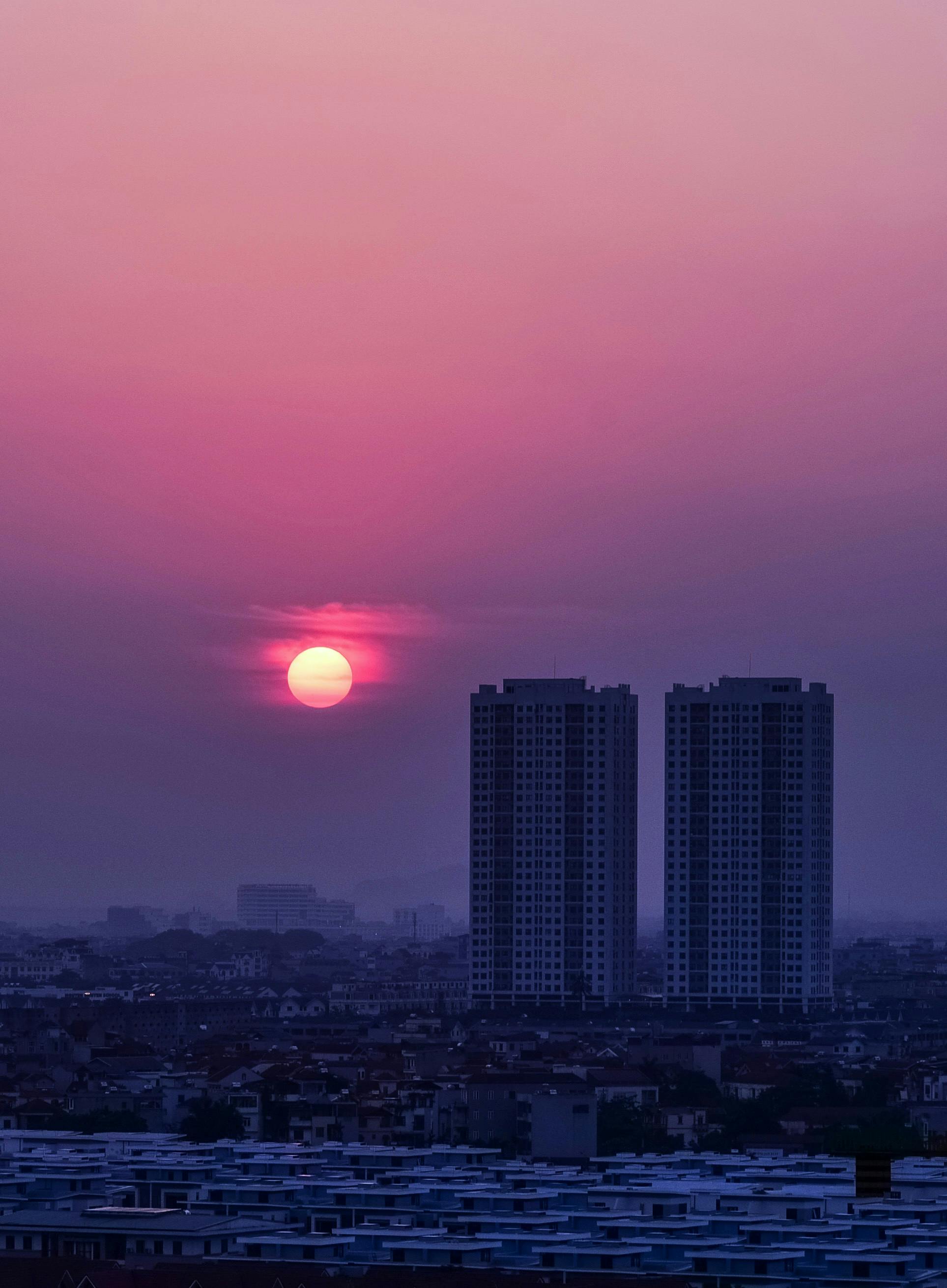 A captivating sunset over a city skyline featuring twin towers under a vibrant purple sky.