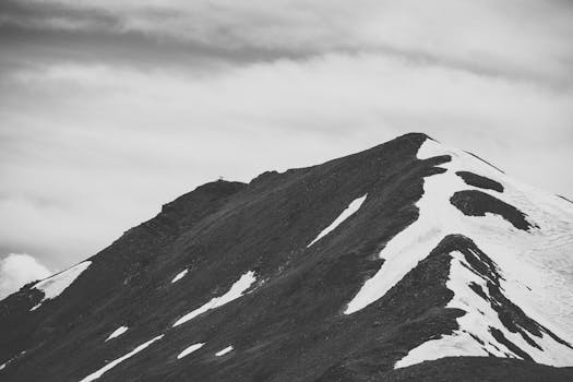 Monochromatic view of a snowy mountain peak under a cloudy sky.