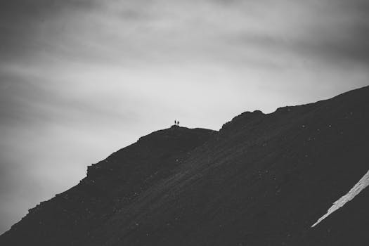 Monochrome image of two hikers standing on a rocky mountain ridge under a cloudy sky.