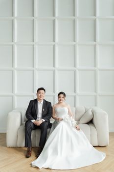 Elegant portrait of a bride and groom seated on a couch indoors, exuding modern sophistication. - Fotografer Sidoarjo