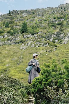 A woman hikes through lush green mountain landscape, enjoying nature.