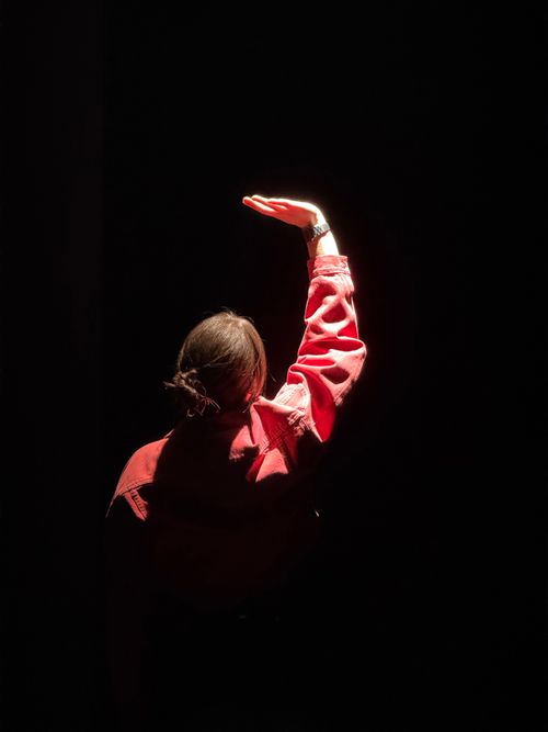Free A woman in a red jacket reaches into a spotlight, creating a dramatic effect. Stock Photo