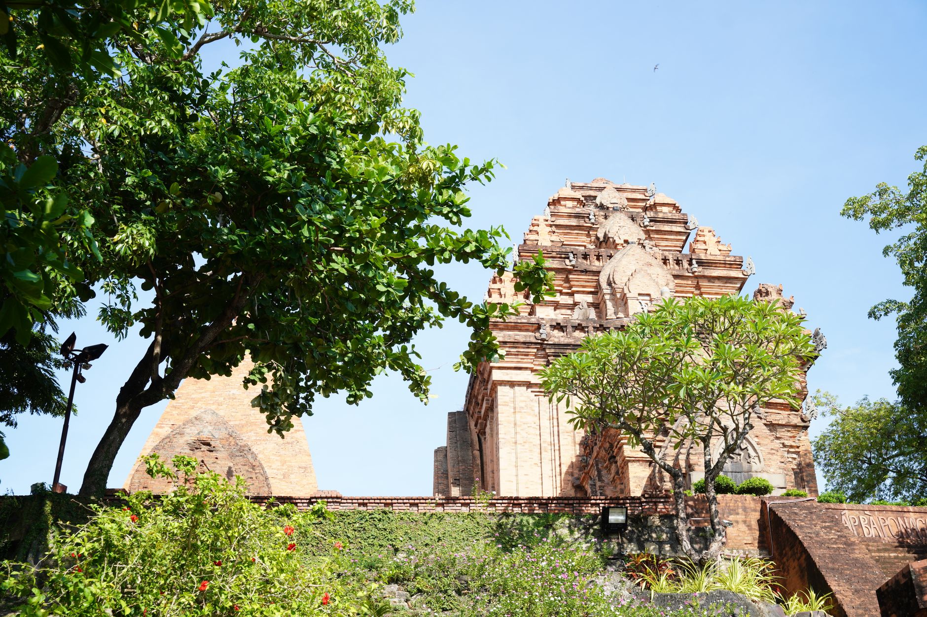 A historic red brick temple amidst vibrant greenery under a clear blue sky showcasing Vietnamese architecture.
