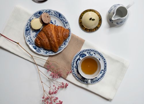 Free Charming arrangement of a croissant, macarons, tea, and fine porcelain on a white backdrop. Stock Photo