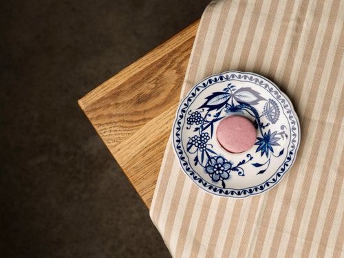 Free Top view of a pink macaron on a decorative porcelain plate, styled on a wooden table. Stock Photo