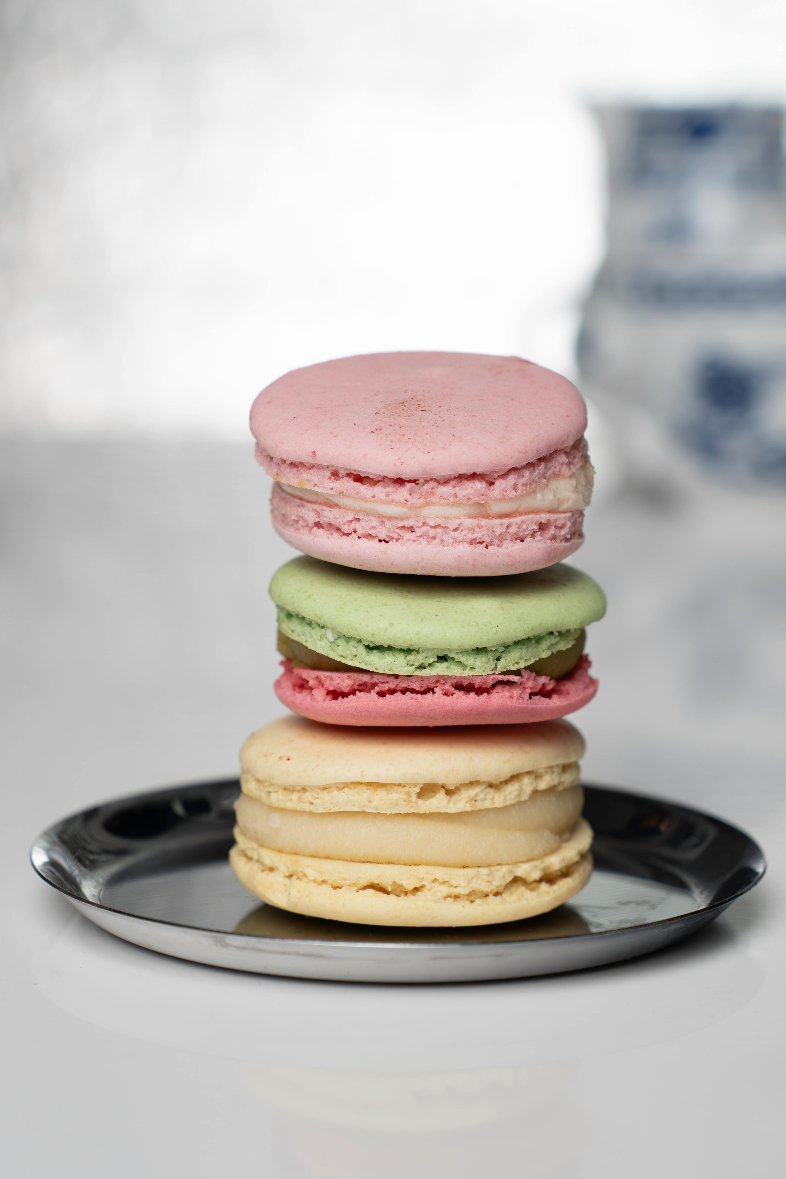 Stacked pink, green, and vanilla macarons on a reflective plate with subtle porcelain backdrop.