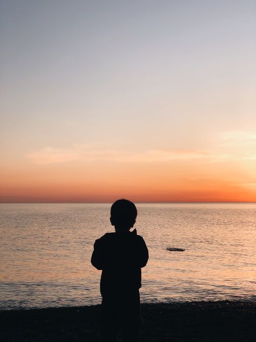 Free Silhouette of a child watching a beautiful sunset over the ocean, creating a peaceful and serene scene. Stock Photo