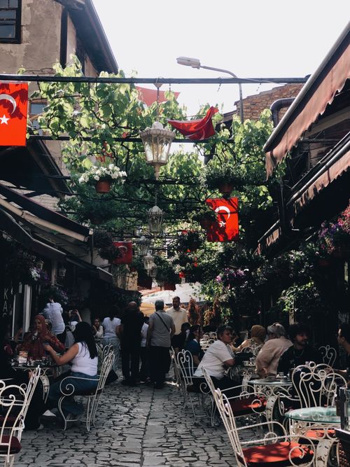 Free Cozy Turkish cafe alley in Istanbul with vibrant flags and relaxing outdoor seating. Stock Photo