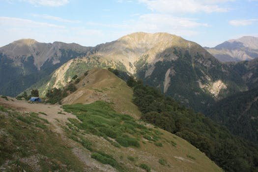 Expansive view of mountainous terrain with lush greenery under a bright sky.