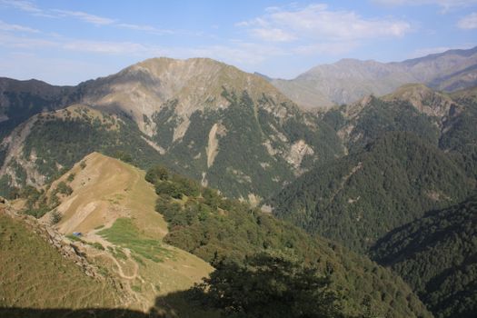 Breathtaking view of mountain ranges with lush green valleys under a clear blue sky.